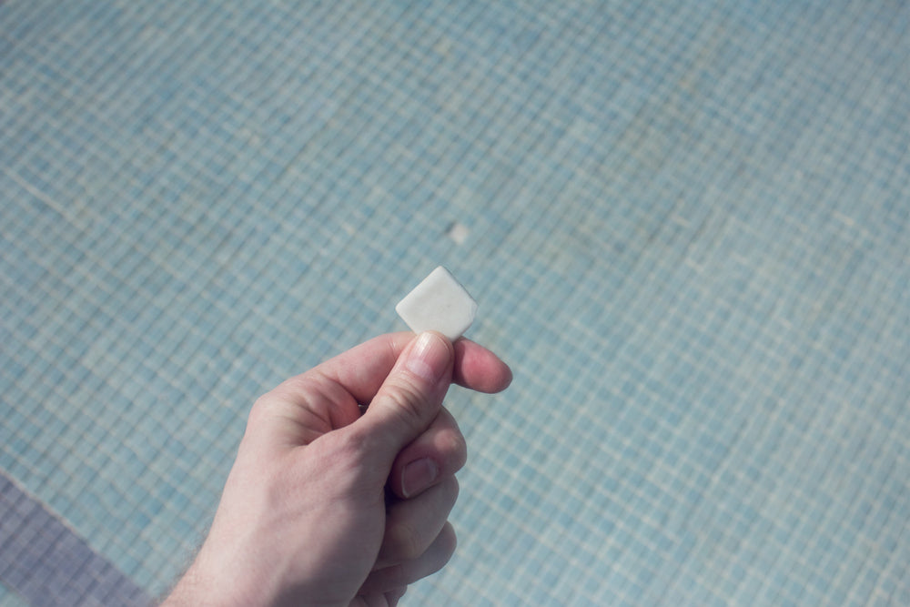 Person Holding a White Pool Tile that Has Fallen Off